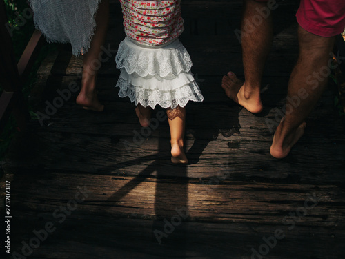 Parents holding daughter toddler walking together. Barefoot legs close up on the way.