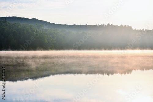 The reflection of a forest across a lake with fog on the surface of the water