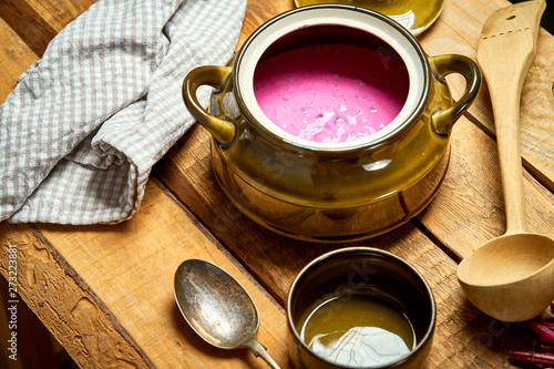 Old vase with cold beetroot soup and spoon on rustic wooden table
