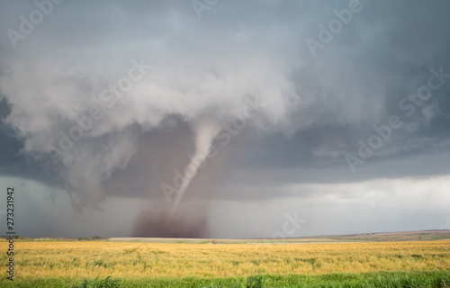 A thin cone tornado spins over the open landscape of the Great Plains.
