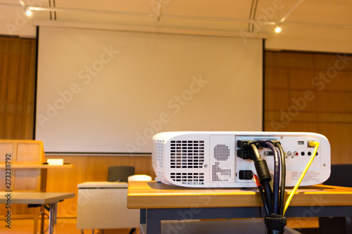 White screen projector in front of a screen in a conference or seminar hall with a white projector screen