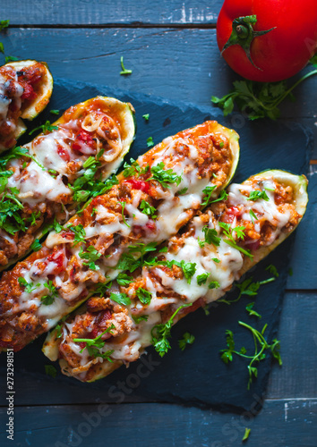 Close-up of stuffed zucchini boats with ground beef, spicy tomato sauce, cheese and fresh parsley, on dark background, top view