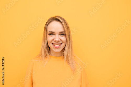 Close-up portrait of a smiling teenage girl on a orange background, wearing a casual clothing, looking into the camera and rejoicing. Positive girl isolated on yellow background.