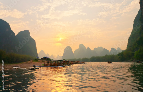 China. Yangshuo. Beautiful Li (Lijiang) River with green karst hills at sunset. Tourists travel along the river on traditional bamboo rafts and admire the setting sun in an unusual natural park