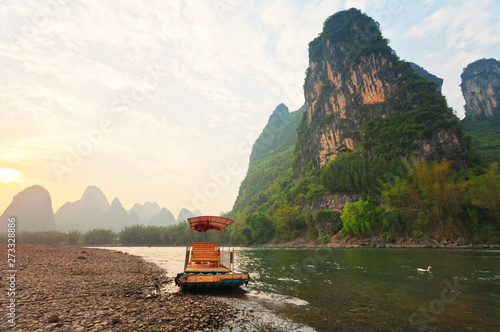 China. The beautiful Li River (Lijiang River) with green karst hills along the banks at sunset. Traditional bamboo pleasure raft waiting for tourists on the stony beach