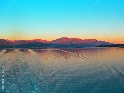 Kotor bay, Montenegro, Europe. Beautiful landscape of the sea, coastline, mountains and sky. View from a cruise ship that leaves a trail of waves on a calm water surface. 