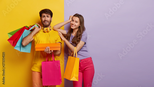 Happy woman satisfied after successful shopping, puzzled man holds many colorful bags and box, make purchase on black Friday, visit shopping mall in day of sales and discounts. Consumerism, purchasing