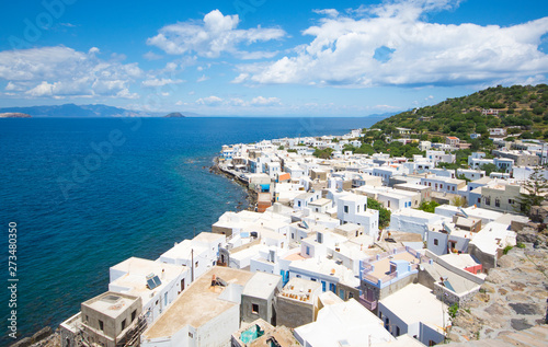 panoramic view from the hill at the Mandrakion city, traditional Greece city whith white houses and blue doors and window shutters between blue sea and green mountains and blue sky in Nisyros Island