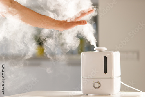 man holds hand over steam aroma oil diffuser on the table at home, steam from the air humidifier, free space. Ultrasonic technology, increase in air humidity indoors, comfortable living conditions