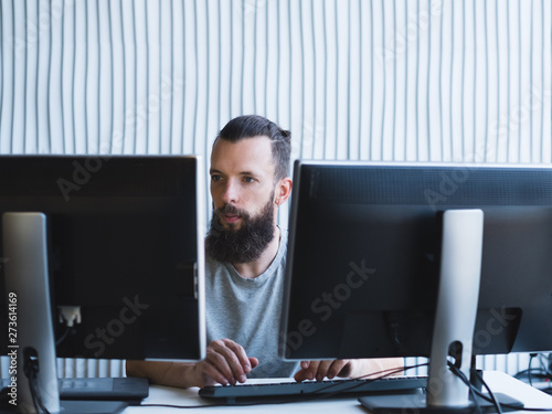 Quality assurance. Bearded software engineer using two monitors, working on task at office. Copy space.