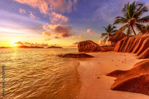Seychelles, La Digue, Anse Source d'Argent at sunset. Landscape with sky and colorful clouds on rock stone of granite with palm trees. Sun at twilight on the calm sea on the horizon.