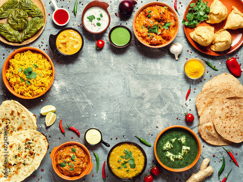Indian cuisine dishes: tikka masala, dal, paneer, samosa, chapati, chutney, spices. Indian food on gray background. Assortment indian meal with copy space for text in center. Top view or flat lay.