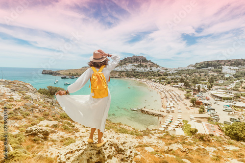 Happy asian woman travels in Greece. Having fun at the stunning view on sea resort and old town of Lindos on the mountain