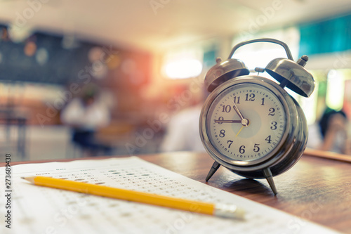 Test Examination in Education concept,pencil and Alarm clock on wooden table,students exams in a classroom background ,Scholarship tests for study abroad