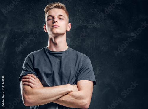 Young arrogant male is looking to the camera crossed his hands over dark background.