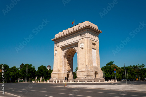 Triumphal Arch, Eastern european landmark and travel destination concept theme with the Arch of Triumph (Arcul de Triumf) in Bucharest (capital city of Romania) against cloudless sky on a summer day