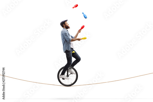 Male juggler with clubs riding a unicycle on a rope