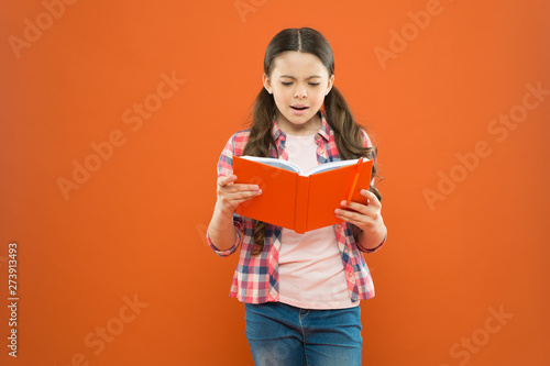 Shes a true bookworm. Adorable small child reading book on orange background. Cute little girl reading for fun. Developing reading ability in school age children. Reading comprehension and fluency