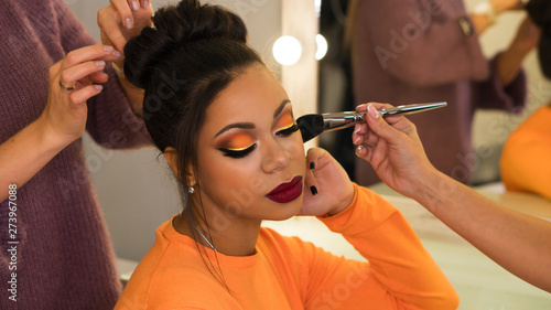Hairstylist and make-up artist makeup and updo for stylish young African-American woman in beauty parlor. Rich colors. Party image. Beauty industry