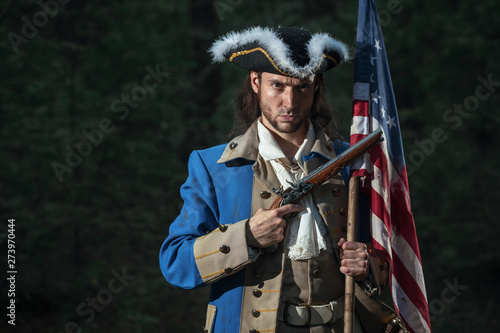 Man dressed as soldier of War of Independence United States aims from pistol with flag. 4 july independence day of USA concept photo composition: soldier and flag.