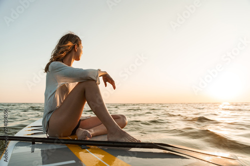 Beautiful young woman sitting on a stand up paddle board