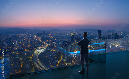 Businessman standing on open roof top balcony watching city night view . Business ambition and vision concept .