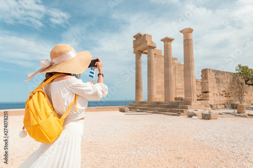 Tourist girl taking photos and selfie of tourist landmark of ancient Acropolis town. Travel destinations and sightseeing tours