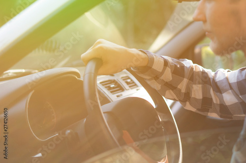 young casual man in checkered shirt driving a car during the sunset