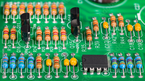 Colored electronic components. Resistors, transistors, capacitors and integrated circuit on PCB. Standard color code. Green copper board detail. Dismantled computer hardware. Electrotechnics, e-waste.