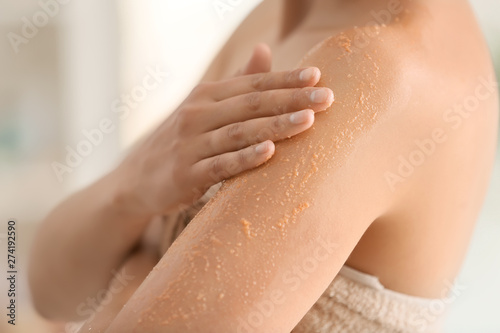 Beautiful young woman applying body scrub at home, closeup