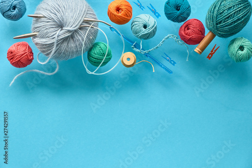 Various wool yarn, knitting needles and stuffed heart on mint colored paper background