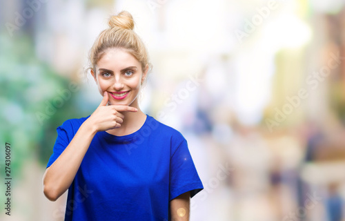 Young beautiful blonde and blue eyes woman wearing blue t-shirt over isolated background looking confident at the camera with smile with crossed arms and hand raised on chin. Thinking positive.
