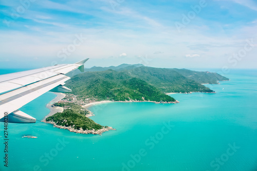 Aerial view of airplane flying above clouds and sky. Airplane wing fly over tropical green island. View from the plane window.