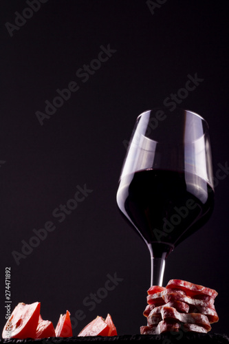 plano contrapicado de una copa de vino tinto con salame troceado y trozos de tomate fresco