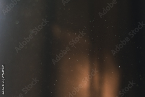 Flying dust at home in the sun on a background of dark curtains.