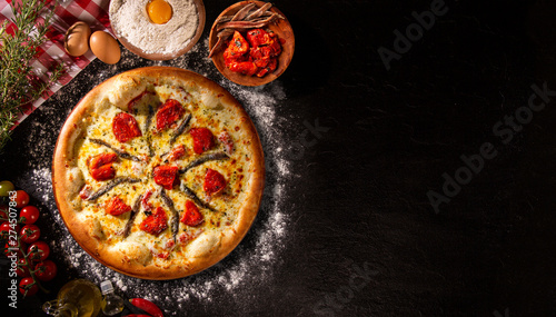 Pizza anchovy and dried tomato on black concrete background. Top view, close up. Traditional Brazilian Pizza.
