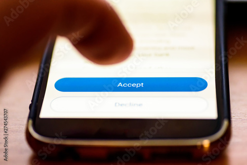 Accept button on smartphone screen closeup with human finger pointing to it