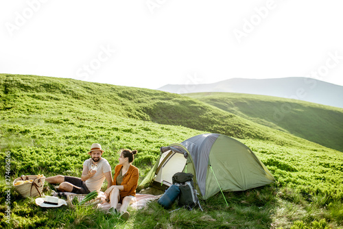 Young and cheerful couple having a picnic at the campsite while traveling high in the mountains during the sunset
