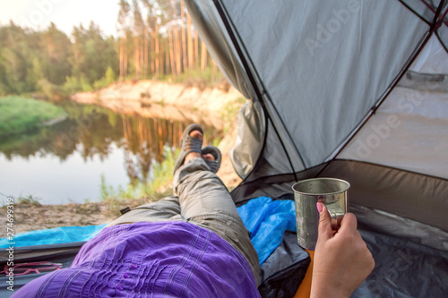 Feet woman relaxing enjoying coffee. River view from tent camping entrance. Travel concept adventure vacations outdoor