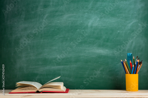 Education and reading concept - group of colorful books on the wooden table in the classroom, blackboard background