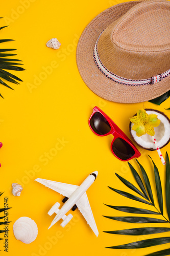 Hat, tropical palm leaves, sunglasses, sea shells on yellow background.
