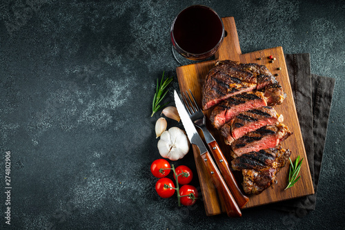 Sliced steak ribeye, grilled with pepper, garlic, salt and thyme served on a wooden cutting Board on a dark stone background. Top view with copy space. Flat lay