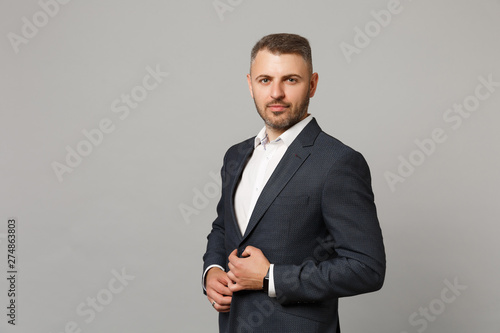Handsome successful confident young business man in classic black suit shirt posing isolated on grey wall background, studio portrait. Achievement career wealth business concept. Mock up copy space.