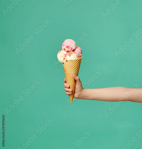 Baby kid hand holding big ice-cream in waffles cone on blue