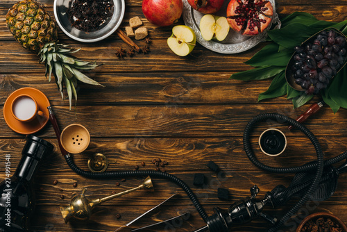 top view of tobacco, hookah, coals, cinnamon, cup of milk and exotic fruits on wooden surface