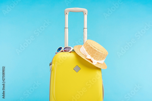 yellow colorful travel bag with straw hat and sunglasses isolated on blue