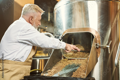 Brewery worker getting spent grain with shovel.