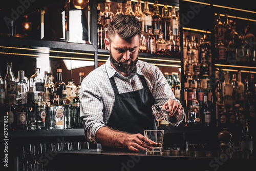 Diligent serious barman is preparing alcoholic beverege for customer.