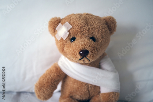 Sad bear doll lying sick in bed with the wound on the head and bandage