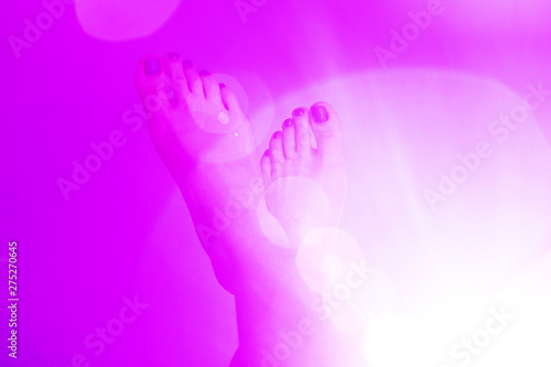 A pair of the woman`s feet on a pink color background with a round halo-effect lights